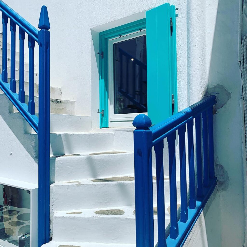 white washed staircase with brilliant blue railing and aqua blue window shutters in Mykonos, Greece