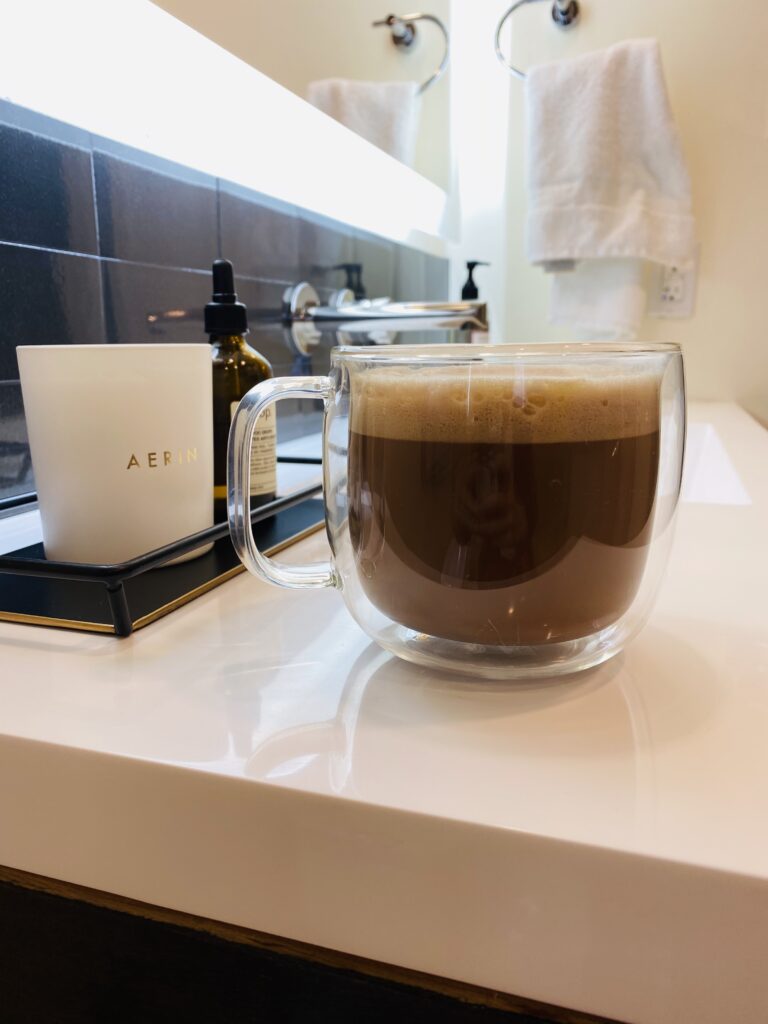 Zwilling J. A. Henckels double glass walled cappuccino mug in bathroom with white countertops and black tile backsplash with Aerin candle on black dish