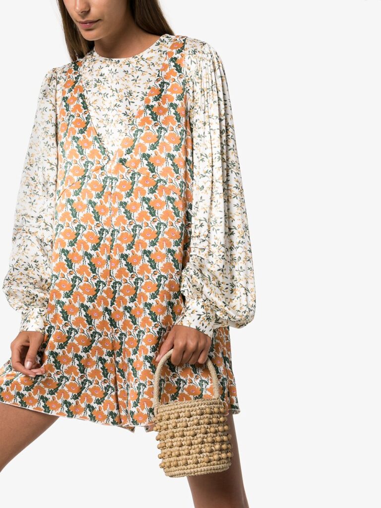model wearing a orange and grey floral dress with white floral puff long sleeves holding a top handle woven bucket bag with woven bead embellishment